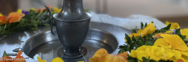Taufstein mit Blumenkranz und Wasserkrug